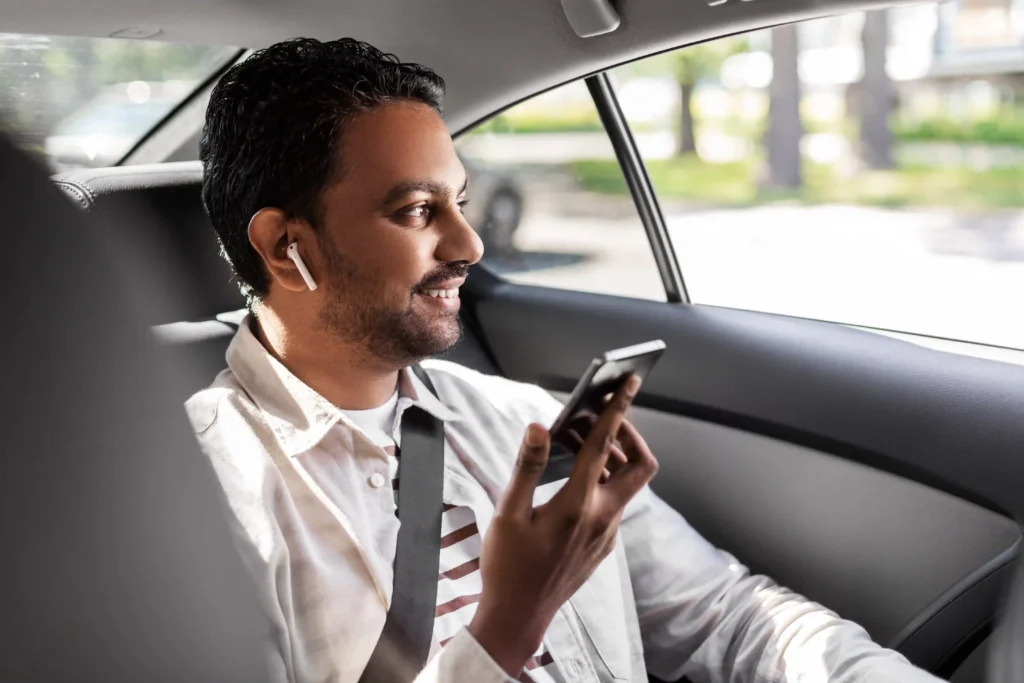 Happy smiling businessman in a suit sitting in a modern car, using a smartphone.